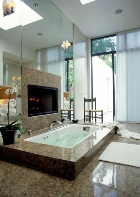 a modern bathroom with a mirror wall, a sunken bathtub clad with tiles, a built-in fireplace and a glazed wall with a curtain