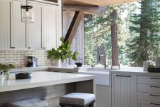 a modern farmhouse kitchen with ivory planked cabinets, a large kitchen island and a glazed wall that can be removed to connect to the forest