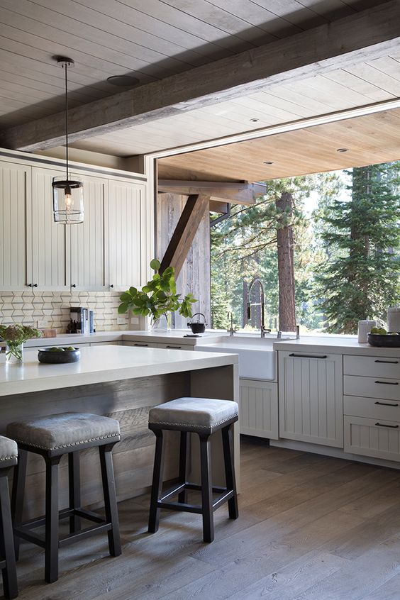 a modern farmhouse kitchen with ivory planked cabinets, a large kitchen island and a glazed wall that can be removed to connect to the forest