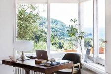 a modern home office with a corner window, a stained wooden desk and a chair, potted plants and lovely views of the sea