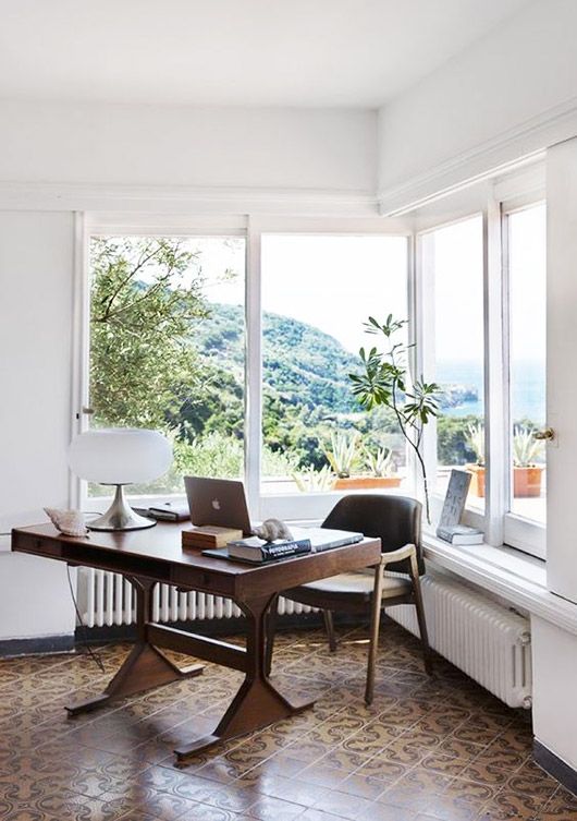 a modern home office with a corner window, a stained wooden desk and a chair, potted plants and lovely views of the sea