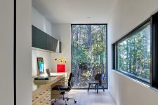 a modern home office with a glazed wall and a long and narrow window, a large desk, black chairs, a sleek storage unit and amazing views of the forest