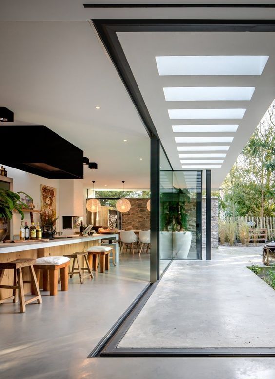 a modern kitchen with an extended kitchen island and mismatching stools, a glass wall that can be partially removed