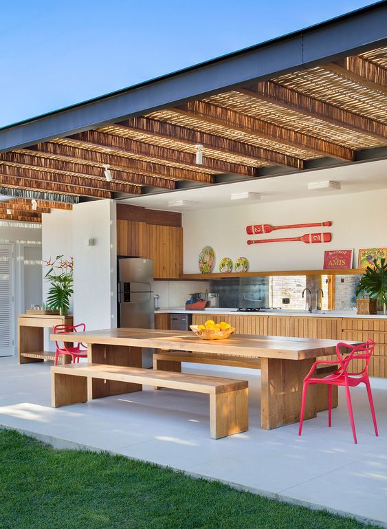 a modern kitchen with slatted cabinets, a mirror backsplash, a dining zone with stained furniture and pink chairs that can be opened to outdoors fully