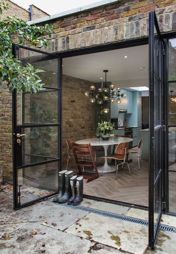 a modern neutral kitchen with an elegant dining zone with an oval table, stained and plywood chairs and modern glass doors to open the space to outdoors