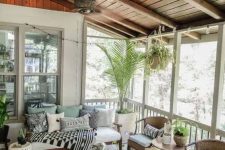 a modern screened patio with wicker and wooden furniture with neutral and pastel upholstery and printed textiles, potted greenery and a view