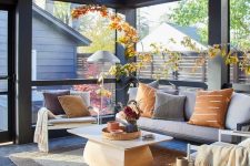 a modern screened porch with a grey modern sofa, white chairs, a coffee table and stained stool and some bright foliage