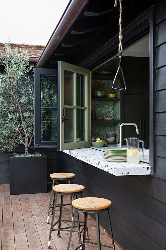 a pass through window with a terazzo windowsill and tall stools and a folding window itself that allows to enjoy meals and drinks outdoors