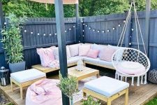 a pretty and lovely terrace wiht a wooden deck, a corner sofa with pastel pillows and blankets, a pink pouf, side tables and potted blooms