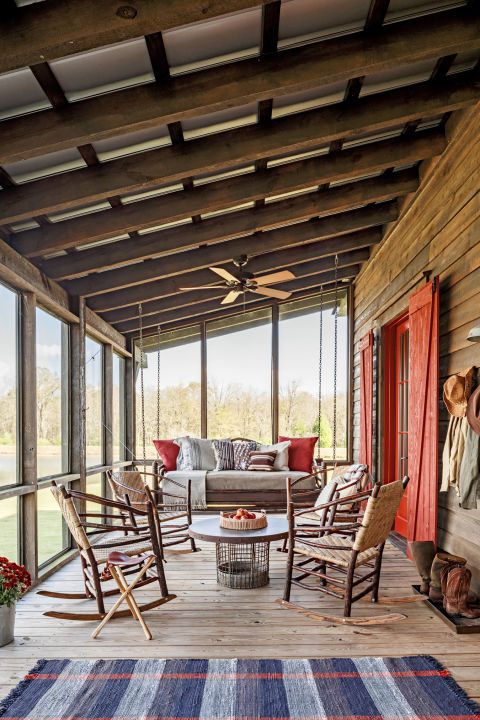 a rustic screened patio with a hanging daybed, a round coffee table and woven rockers, a bold rug and printed pillows