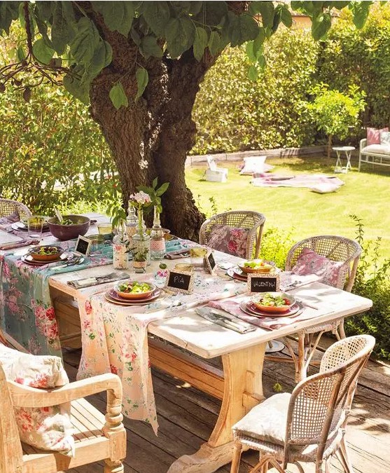 a rustic spring terrace with a wooden table and wicker chairs, with floral runners and napkins set for a party
