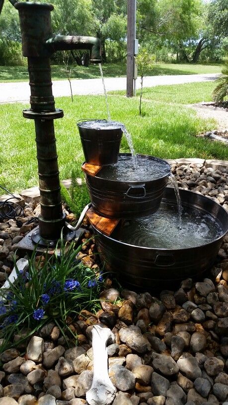 a rustic tiered fountain with galvanized buckets and bathtubs plus pebbles and blooms around is amazing