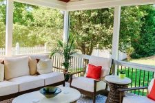 a screened patio with white seating furniture, coffee and side tables, bright pillows, greenery and a large printed rug