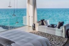 a sea bedroom with glass walls and amazing views, chic white furniture, pendant lamps and a pebble rug is fantastic