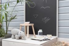 a simple Nordic outdoor play space with a chalkboard, a reading nook, a small sand box and a deck with toys