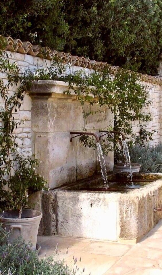 a simple and stylish fountain of two faucets and a bathtub of stone, with greenery around is amazing