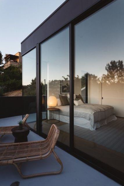 a simple contemporary bedroom with a bed, a nightstand with a lamp and glass walls plus an entrance to the terrace is very cool