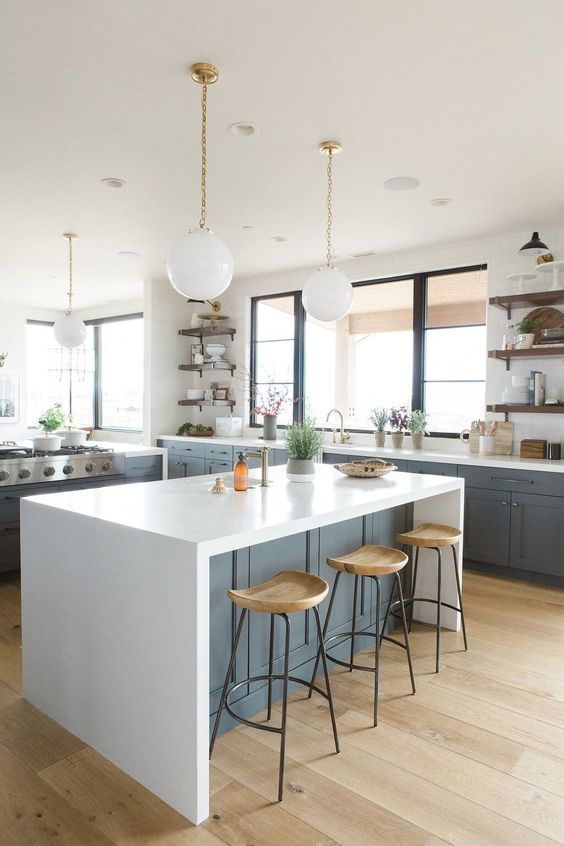 a slate grey farmhouse kitchen with white stone countertops, round pendant lamps and large windows with views