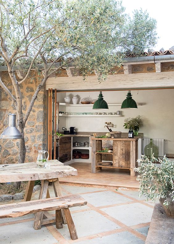 a small and lovely rustic kitchen with wooden cabinets and a folding glass wall that allows to enjoy an outdoor space
