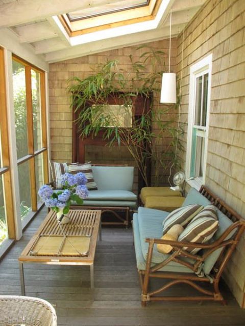 a small colorful screened patio with rattan sofas with blue upholstery, a coffee table, greenery and a pendant lamp