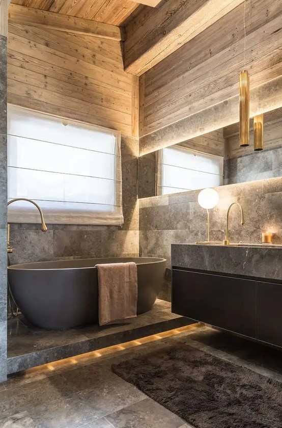 a sophisticated chalet bathroom clad with grey stone tiles, with wood, a black floating vanity with a large sink, an oval tub and lights