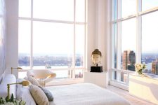 a stunning neutral bedroom with some cabinets, a bed, tree stumps, a bet chair and glass walls with the views of a big city