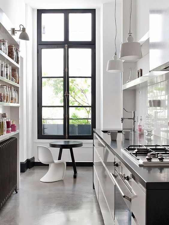 a stylish kitchen with white walls and black cabinets, black stone countertops, white pendant lamps and a chic tall window with a garden view