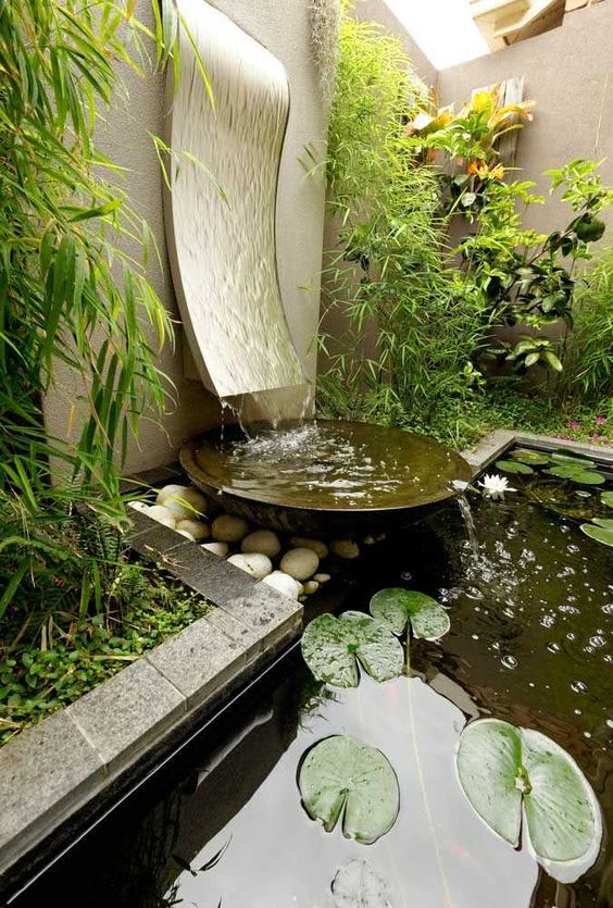 un joli étang dans la cour une fontaine moderne et élégante avec une vague qui descend et un bol en métal ainsi qu'un étang supplémentaire avec des roches et des galets