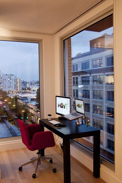 a tiny and cool home offic enook with glazed walls and big city views, a black desk and a red chair is a lovely space to work and enjoy the views