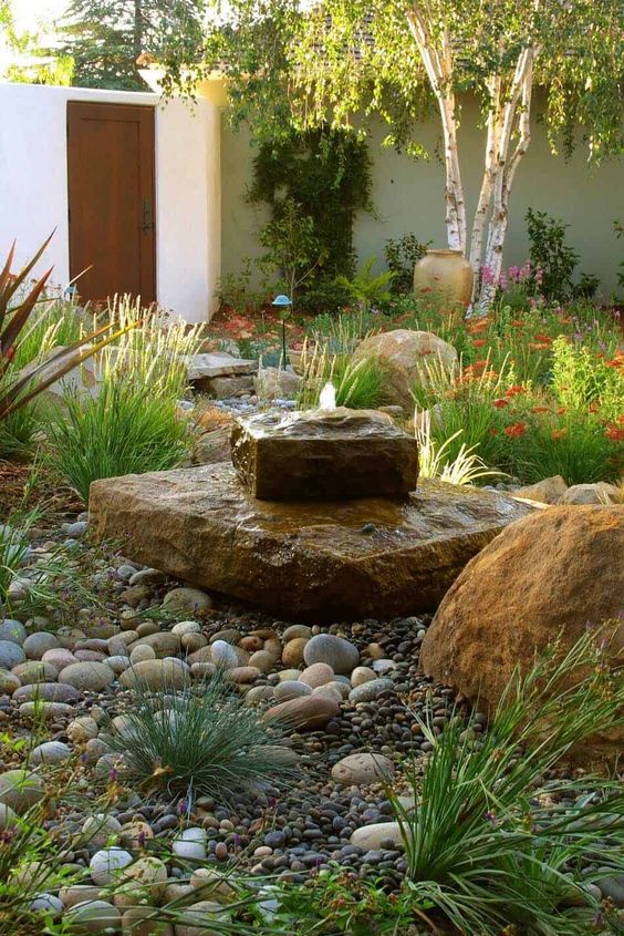 a unique and bold stone slab fountain, landscaping and pebbles around create a gorgeous look in the garden