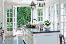 a vintage farmhouse garden with white shaker style cabinets, black stone countertops, elegant lamps and glazed walls with garden views
