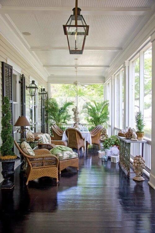 a vintage inspired screened porch with wicker furniture and printed upholstery, potted plants and decor and lanterns