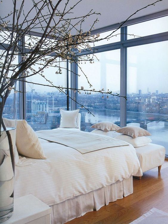 an elegant modern bedroom with a bed, an upholstered bench, some nightstands and glass walls to enjoy the views of the city