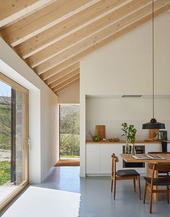 an elegant modern kitchen with sleek neutral cabinets, a chic dining zone with a stained table and black chairs and a glass wall with a sliding door