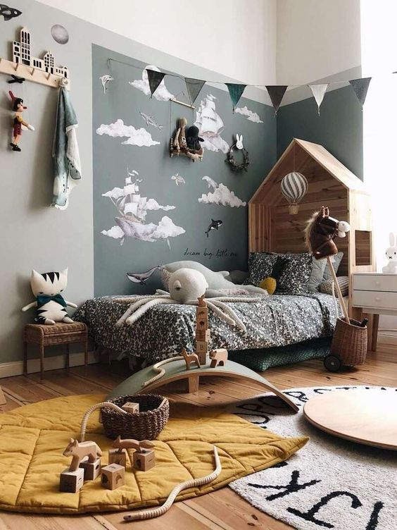 a Nordic kid's bedroom with an accent corner, a wooden house shaped bed with printed bedding, layered rugs, buntings and racks