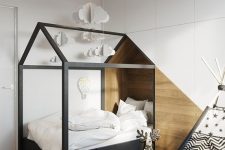 a Nordic kids’ room with a black house-shaped bed in a niche, a teepee, a sleek storage unit that covers the whole wall