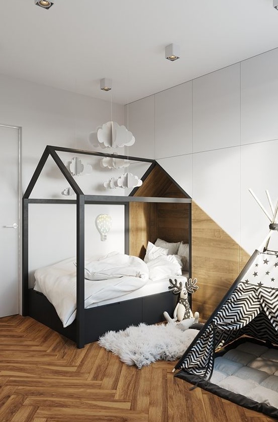 a Nordic kids' room with a black house-shaped bed in a niche, a teepee, a sleek storage unit that covers the whole wall