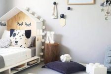 a Nordic kid’s room with a house-shaped bed with storage, a stump, pillows, wall decor and a map rug for playing
