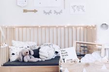 a Nordic kid’s room with a wooden bed and a wooden box for toys, a printed rug, a gallery wall with artworks and not only