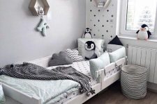a Nordic kid’s room with an accent wall, a white bed with pastel bedding, a fabric basket and hexagon-shaped wall-mounted shelves