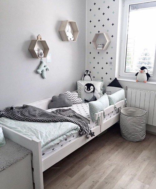 a Nordic kid's room with an accent wall, a white bed with pastel bedding, a fabric basket and hexagon-shaped wall-mounted shelves