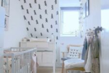 a Nordic nursery with a fir tree wall, a black and white can, neutral furniture and some artworks for an ambience