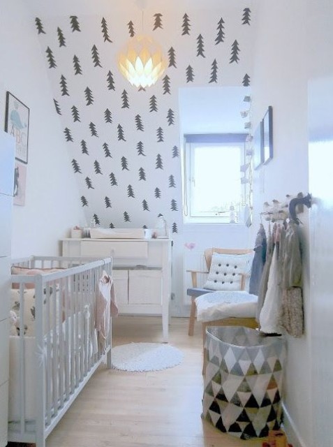 a Nordic nursery with a fir tree wall, a black and white can, neutral furniture and some artworks for an ambience