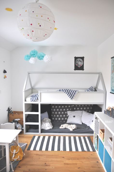 a Scandi kids' room with a bunk bed, printed bedding, a striped rug, a white table and chair, a white storage unit