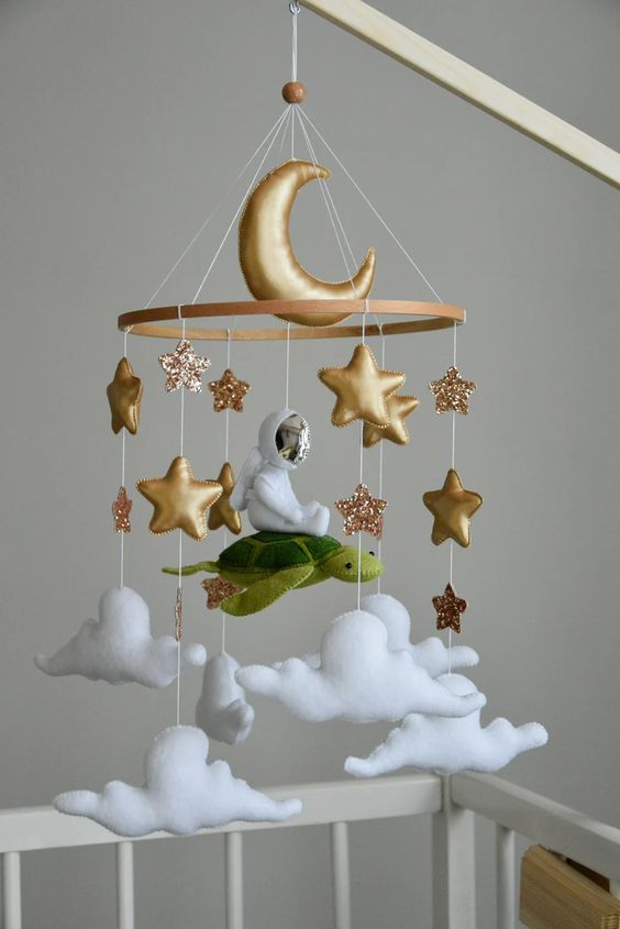 a beautiful and inspiring mobile with gold stars and a moon, an astronaut flying on a turtle and clouds is a super cool idea