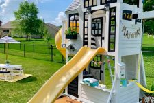a beautiful black and white kids’ playhouse with black window frames, with a small space inside, a yellow slide and another one on the other wall