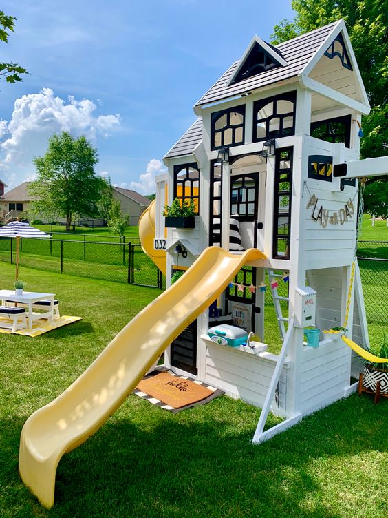 a beautiful black and white kids' playhouse with black window frames, with a small space inside, a yellow slide and another one on the other wall