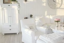 a beautiful white shabby chic living room with stylish vintage furniture, a clock, a chandelier and greenery in pots