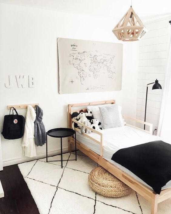 a black and white Scandi kid's room with a stained bed, black and white bedding, a black table, black and white rugs and a jute pouf