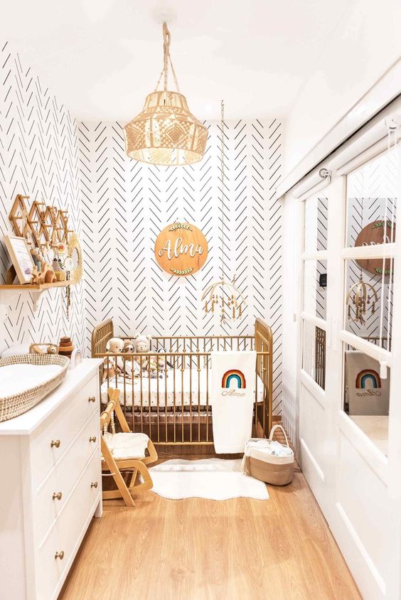 a boho neutral nursery with a gilded crib, a white dresser that is a changing table, some baby furniture and a wall-mounted shelf